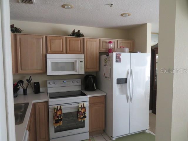 A kitchen features light wood cabinets, white appliances, and a stainless steel sink — 1188 N FAIRWAY DRIVE UNIT 1188, APOPKA, FL
