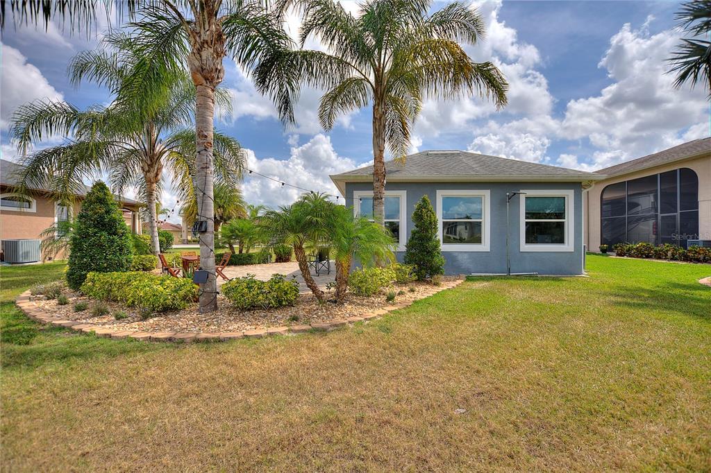 A backyard view featuring a blue house, a stone patio, and several palm trees — 544 NARROW POND ROAD, POLK CITY, FL
