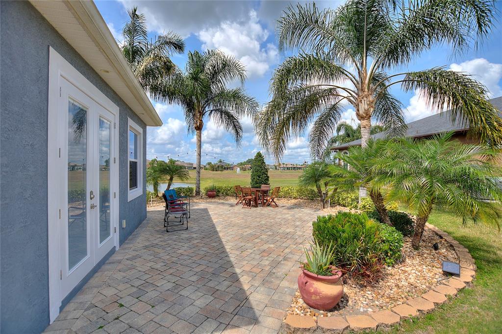 A paved patio with outdoor furniture and palm trees overlooks a grassy field and pond — 544 NARROW POND ROAD, POLK CITY, FL