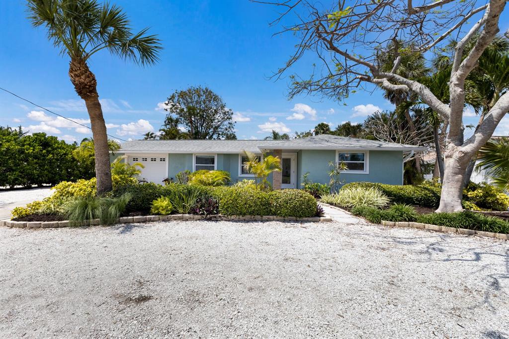 A light green single-story house features a gravel driveway, palm trees, and landscaped garden beds — 506 69TH STREET, HOLMES BEACH, FL