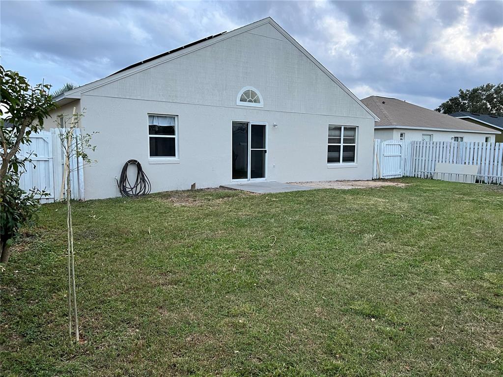 The exterior rear view of a house features a lawn, a patio, and white fencing — 123 OSPREY HEIGHTS DRIVE, WINTER HAVEN, FL