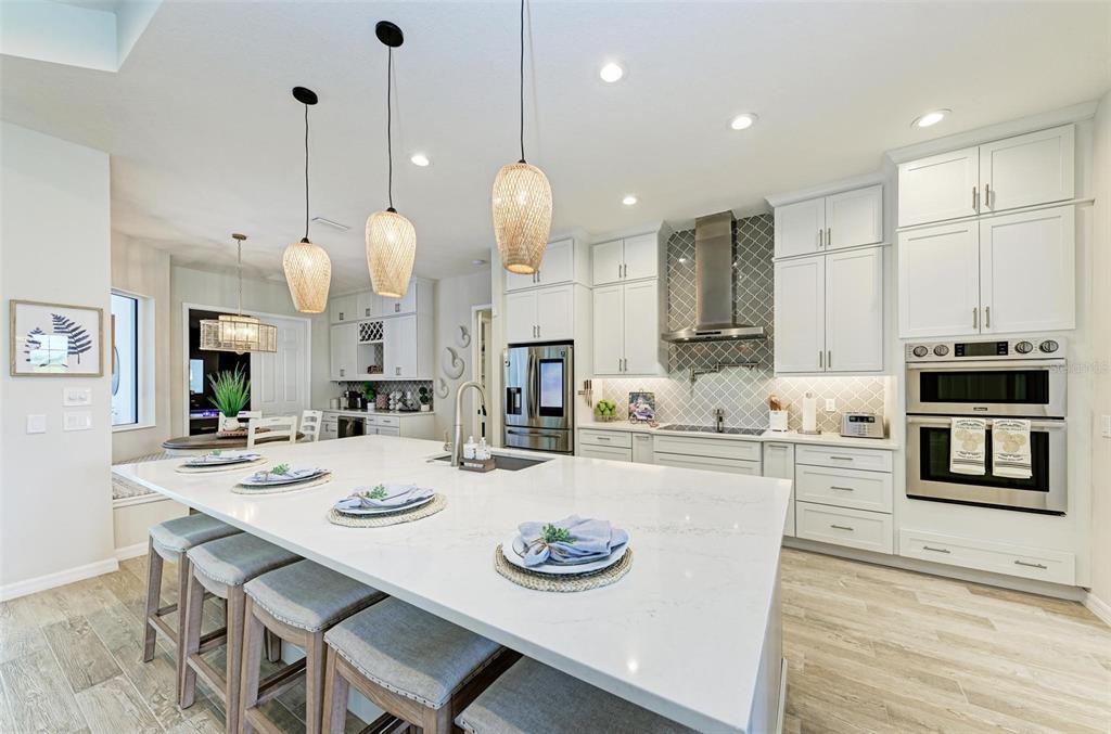A modern kitchen features a large white quartz island, pendant lighting, and stainless steel appliances — 8211 37TH AVENUE CIRCLE W, BRADENTON, FL