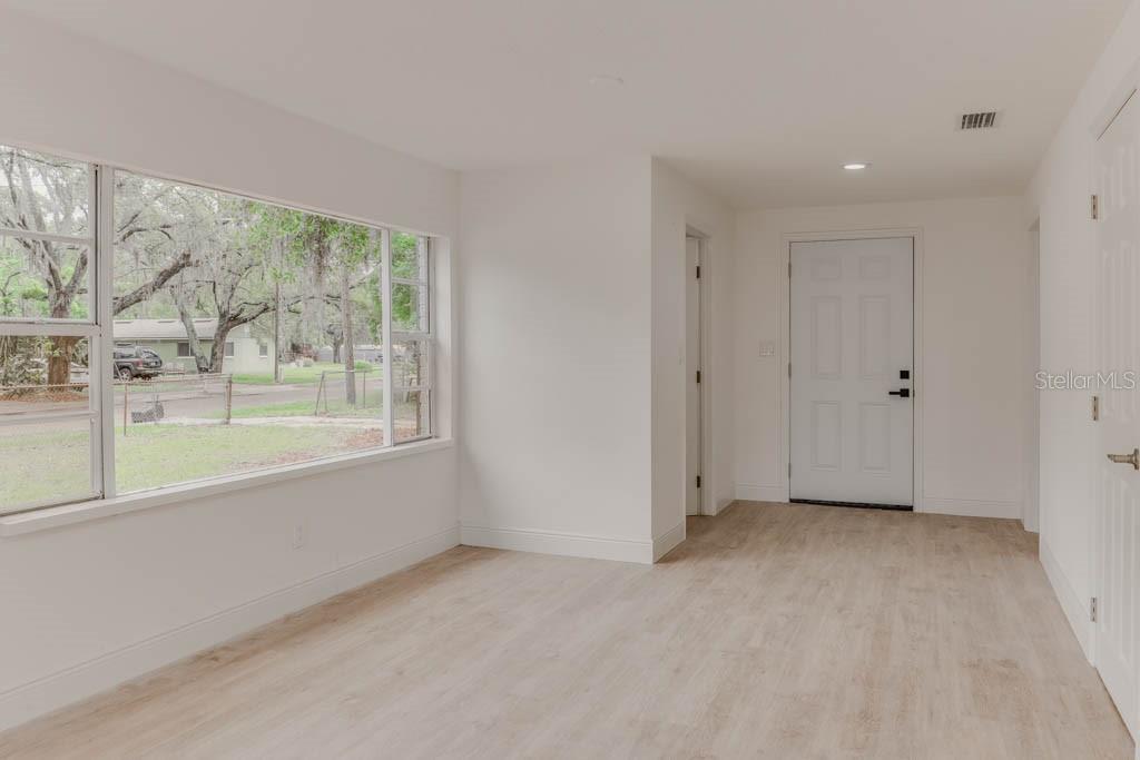 A bright room with light wood-look flooring, white walls, a large window, and an entry door — 1255 PINE STREET, ALTAMONTE SPRINGS, FL