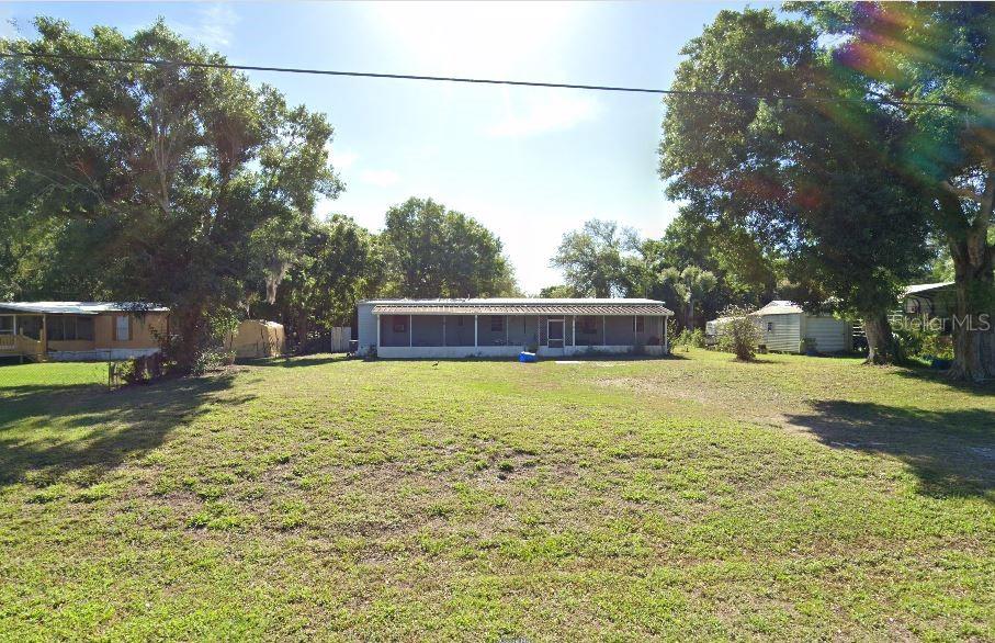 A wide, grassy yard leads to a single-story mobile home with a full-length front porch — 6014 SE 86TH BOULEVARD UNIT 1, OKEECHOBEE, FL