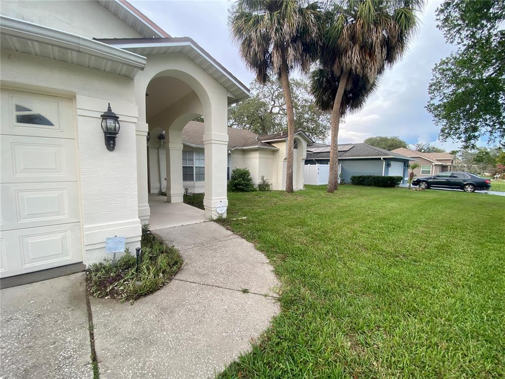 A beige house with a covered entryway, a concrete walkway, and palm trees in the yard — 8201 RHANBUOY ROAD, SPRING HILL, FL