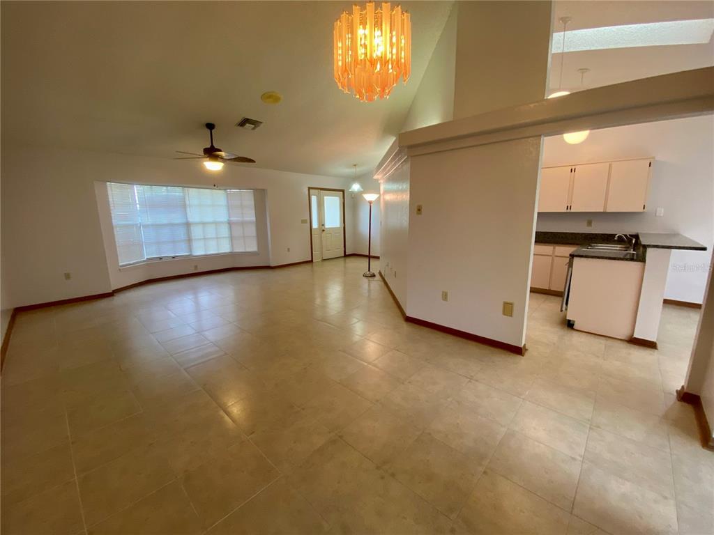 An open-concept living area features tile flooring, a vaulted ceiling, and an adjacent kitchen — 8201 RHANBUOY ROAD, SPRING HILL, FL