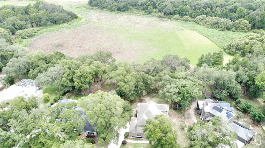 An aerial view shows three houses nestled among trees bordering a large, open field — 1016 LAKESIDE DR. DRIVE, APOPKA, FL