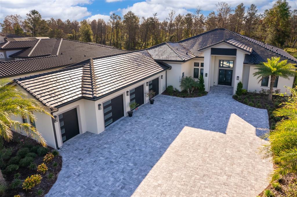 An aerial view of a modern house with a paved driveway and three-car garage — 15144 PENDIO DRIVE, BELLA COLLINA, FL