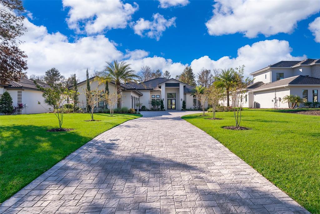 A paved driveway leads to the front entrance of a modern, single-story suburban home — 15144 PENDIO DRIVE, BELLA COLLINA, FL