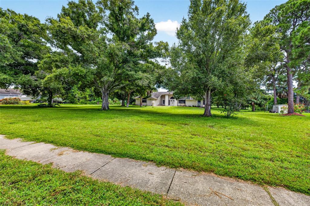 A single-story house sits behind a large, grassy front yard with several mature trees — 6320 66TH AVENUE N, PINELLAS PARK, FL