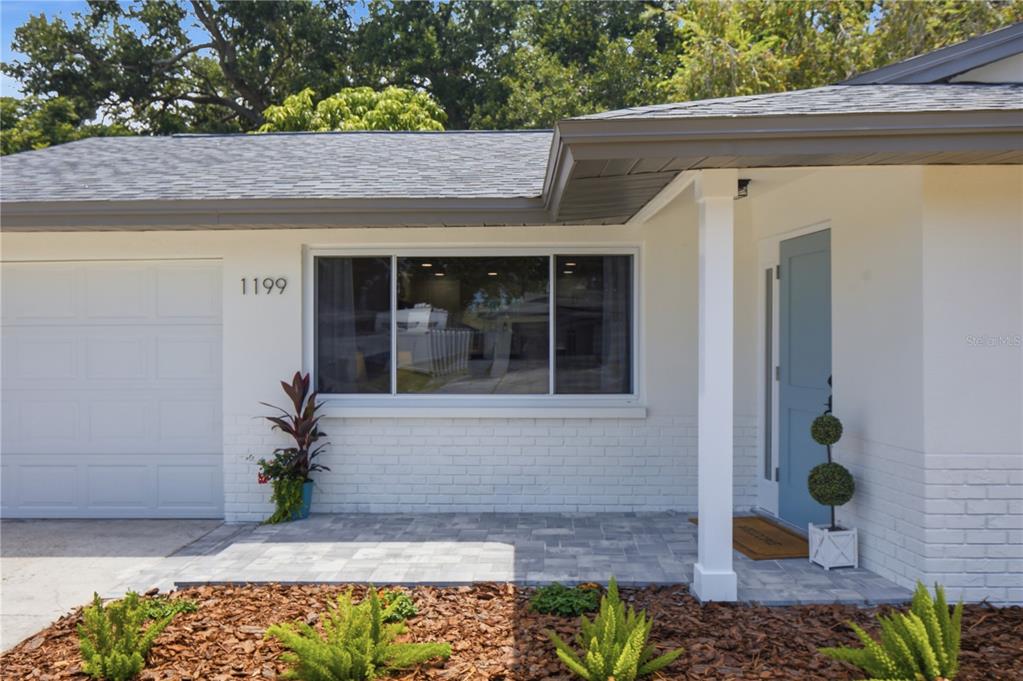 A light blue front door with a side window sits under a covered porch entrance — 1199 KEENE ROAD, DUNEDIN, FL