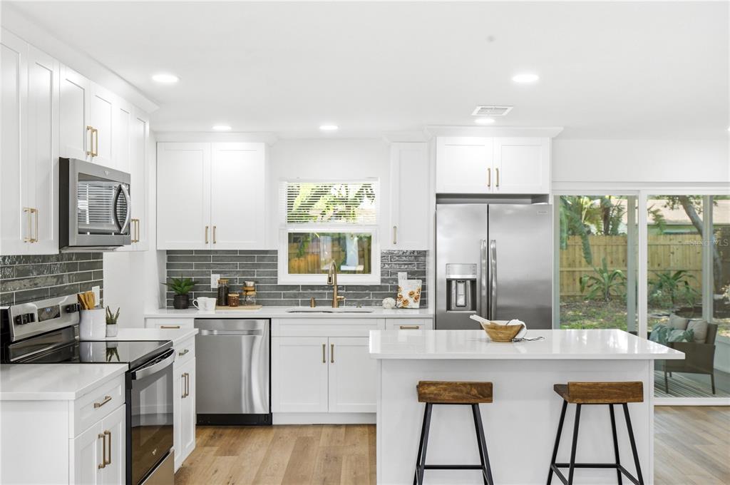 An open-concept living room and kitchen featuring white cabinetry, wood flooring, and neutral furniture — 1199 KEENE ROAD, DUNEDIN, FL
