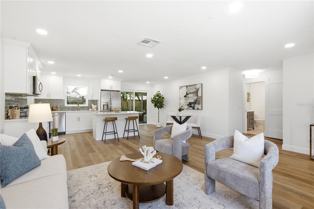 A bright open-concept living room and kitchen featuring white cabinetry, wood flooring, and neutral furniture — 1199 KEENE ROAD, DUNEDIN, FL