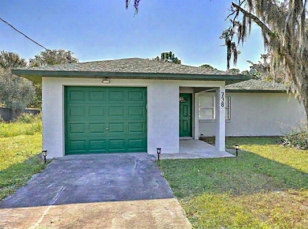 A single-story house with a green garage door, a front porch, and a concrete driveway — 738 LEMANS DRIVE, SEBRING, FL