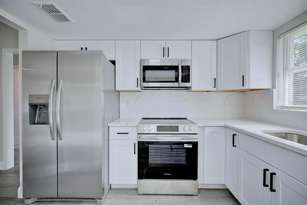 A kitchen features white cabinets, stainless steel appliances, and a marble-patterned backsplash — 738 LEMANS DRIVE, SEBRING, FL