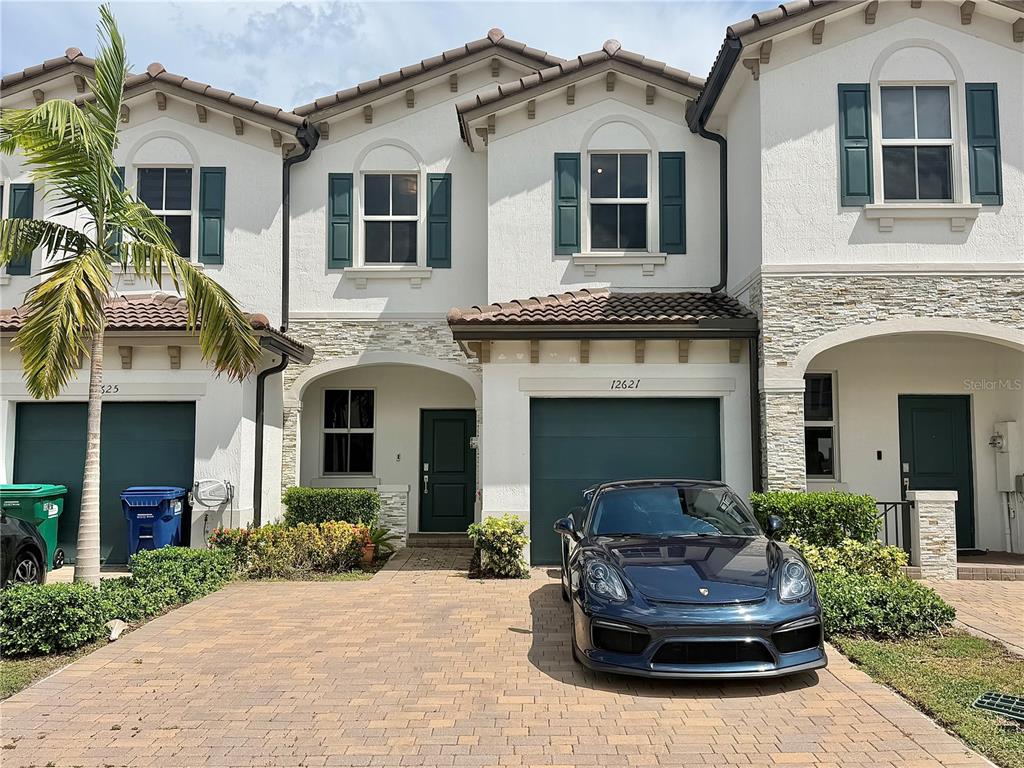 A multi-story townhouse exterior features a paved driveway, a dark car, and green shutters — 12621 NW 23RD PLACE, MIAMI, FL