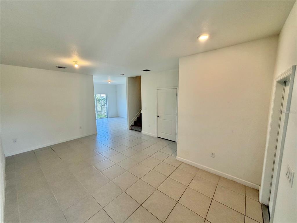 An empty room with white walls and light-colored tile flooring leads to a staircase — 12621 NW 23RD PLACE, MIAMI, FL