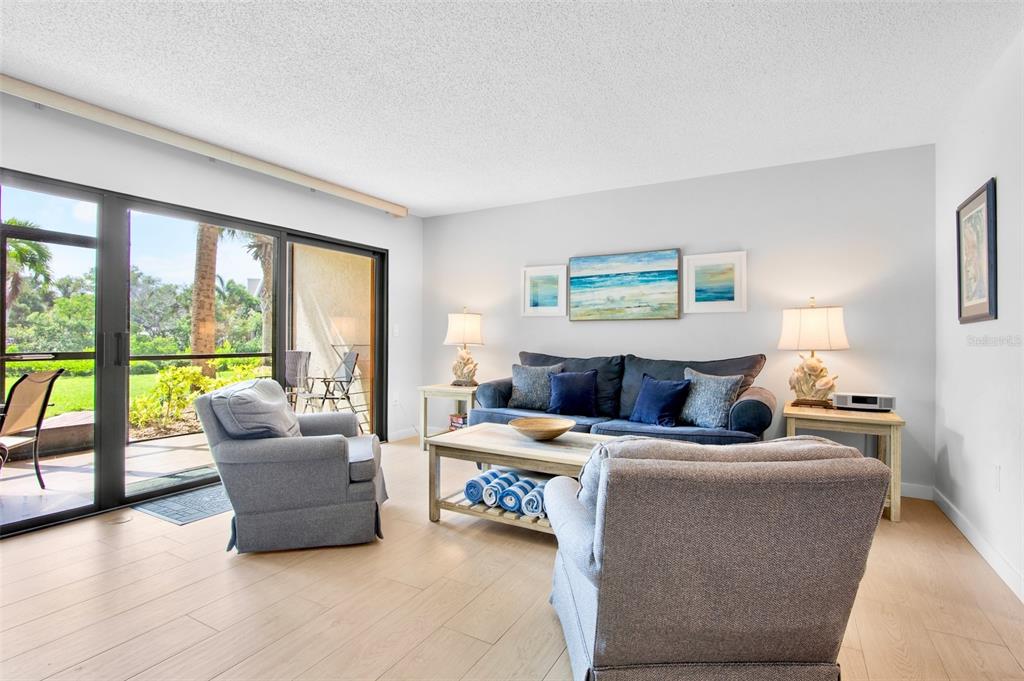 A living room features light wood flooring, a blue sofa, two armchairs, and sliding glass doors — 1600 COVE II PLACE UNIT 412, SARASOTA, FL