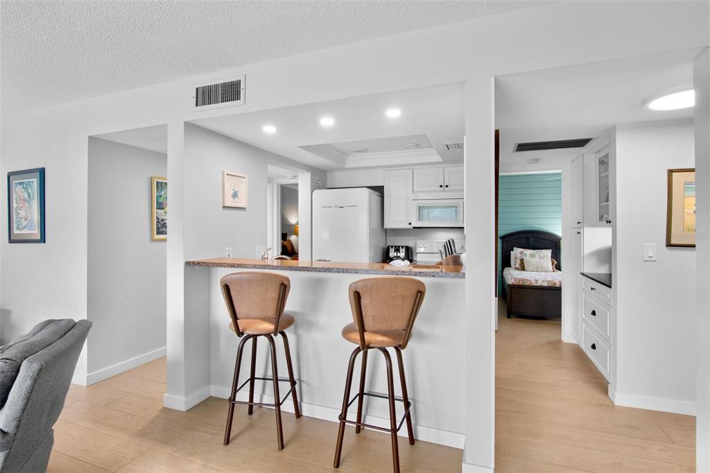 A kitchen with a breakfast bar and two stools overlooks a bedroom with a bed — 1600 COVE II PLACE UNIT 412, SARASOTA, FL