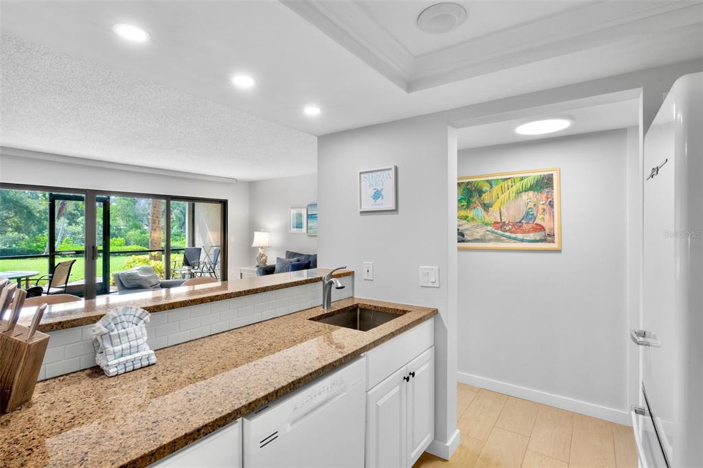 A kitchen with granite countertops, a white dishwasher, and a view into the living area — 1600 COVE II PLACE UNIT 412, SARASOTA, FL
