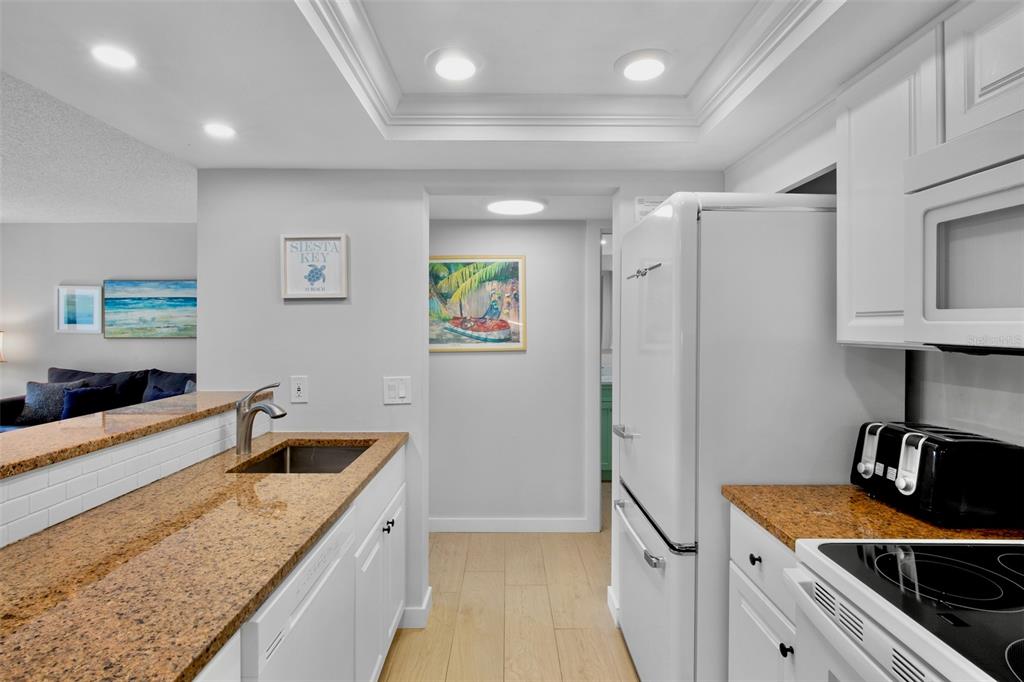 A kitchen features granite countertops, white cabinets, a retro-style refrigerator, and a pass-through breakfast bar — 1600 COVE II PLACE UNIT 412, SARASOTA, FL