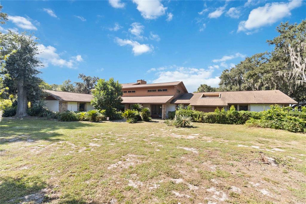 A low-slung, multi-level house with a brown roof sits behind a large grassy yard — 4226 DOWNEAST LANE, WINDERMERE, FL