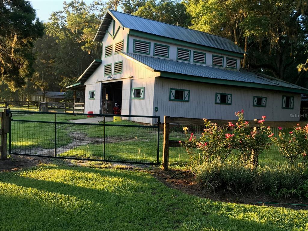 A white barn with a metal roof stands behind a fenced pasture with rose bushes — 15000 W HWY 318, WILLISTON, FL