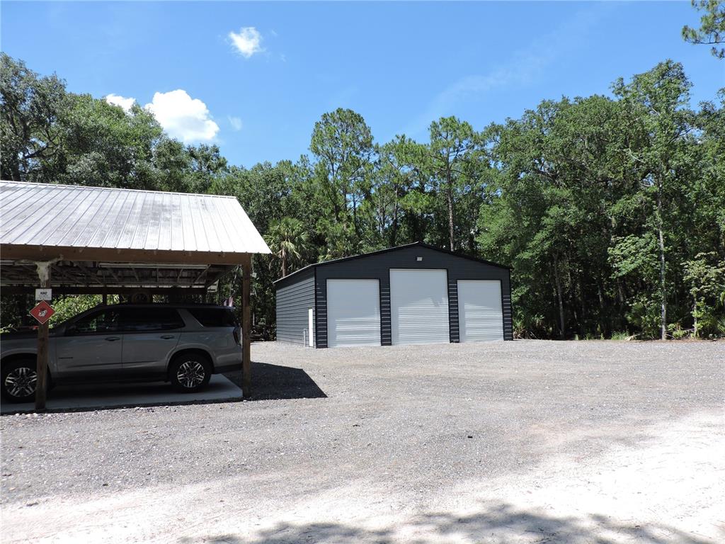 A dark metal garage with three roll-up doors sits on a gravel lot near trees — 400 S COUNTY ROAD 115, BUNNELL, FL