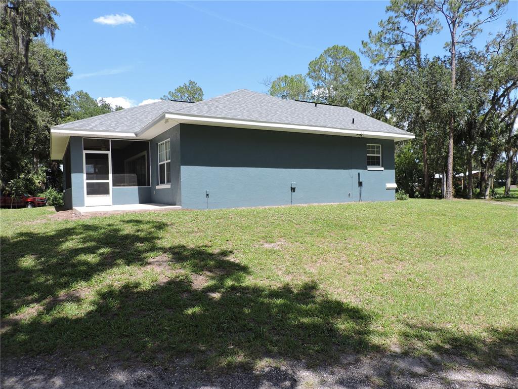 The exterior of a gray house features a screened-in porch and a large grassy backyard — 400 S COUNTY ROAD 115, BUNNELL, FL