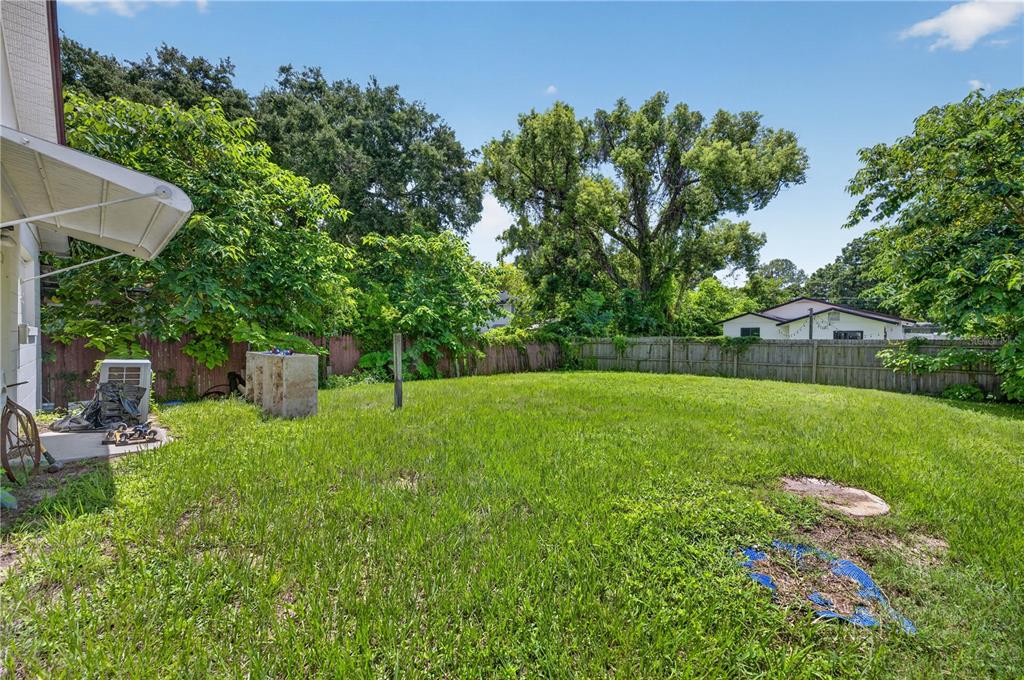 A grassy backyard features a wooden fence, mature trees, and a concrete patio area — 840 NEUSE AVENUE, ORLANDO, FL