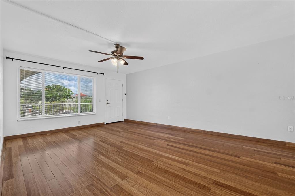 An empty room with hardwood flooring, a ceiling fan, and a large window — 2433 BRAZILIA DRIVE UNIT 49, CLEARWATER, FL