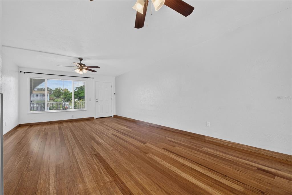 An empty room with hardwood floors, a ceiling fan, and a large window — 2433 BRAZILIA DRIVE UNIT 49, CLEARWATER, FL