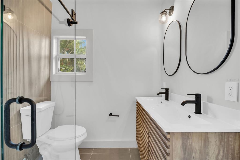A modern bathroom features a double vanity with wood-slat cabinetry, black fixtures, and a glass-enclosed shower — 5355 2ND AVENUE S, ST PETERSBURG, FL