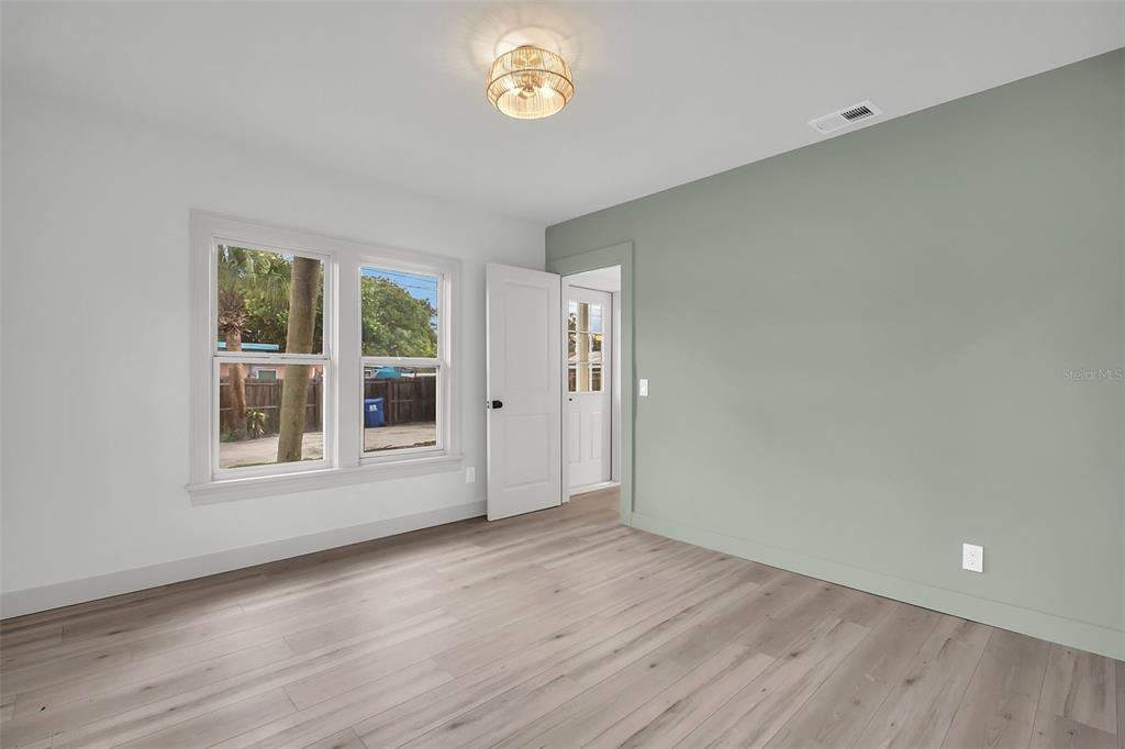 A bedroom with light wood-look flooring, a sage green accent wall, and a white door — 5355 2ND AVENUE S, ST PETERSBURG, FL