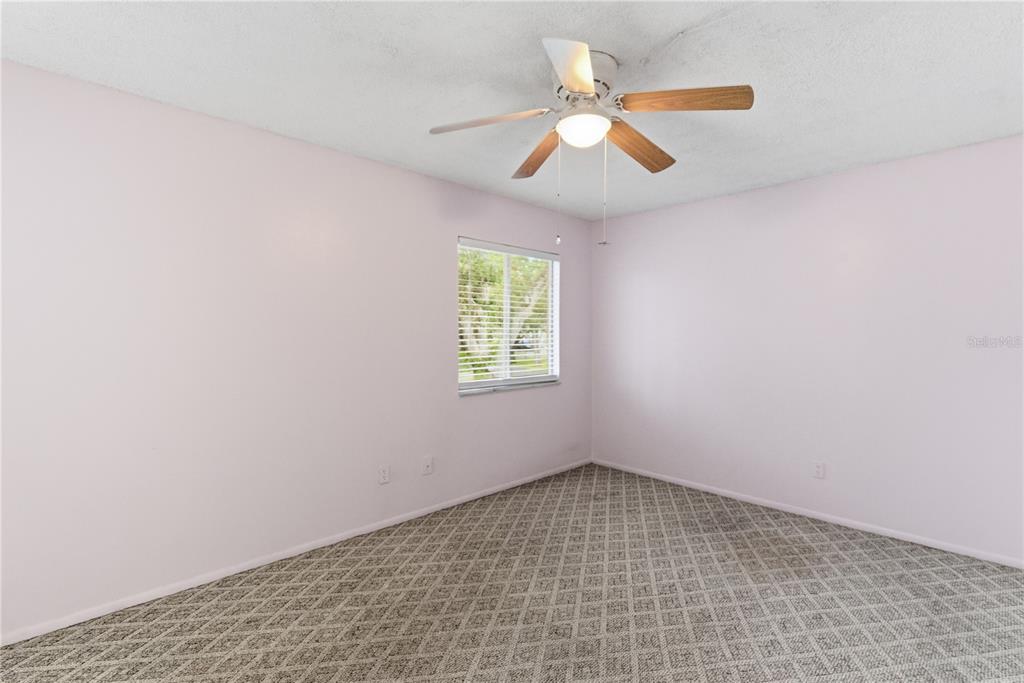 An empty bedroom features light pink walls, patterned gray carpet, and a ceiling fan — 521 MIDWAY DRIVE UNIT B, OCALA, FL