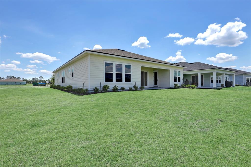 The exterior rear view of a single-story house features light siding and a grassy yard — 71 BRICKSTONE TRACE, ST AUGUSTINE, FL