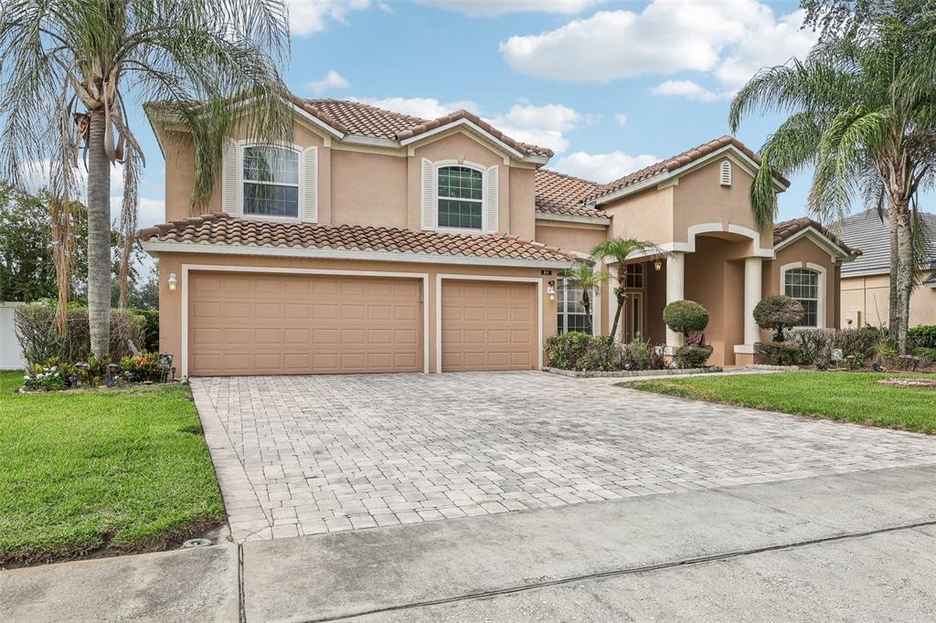 A two-story stucco house with a tile roof, three-car garage, and a paved driveway — 84 BRAELOCK DRIVE, OCOEE, FL