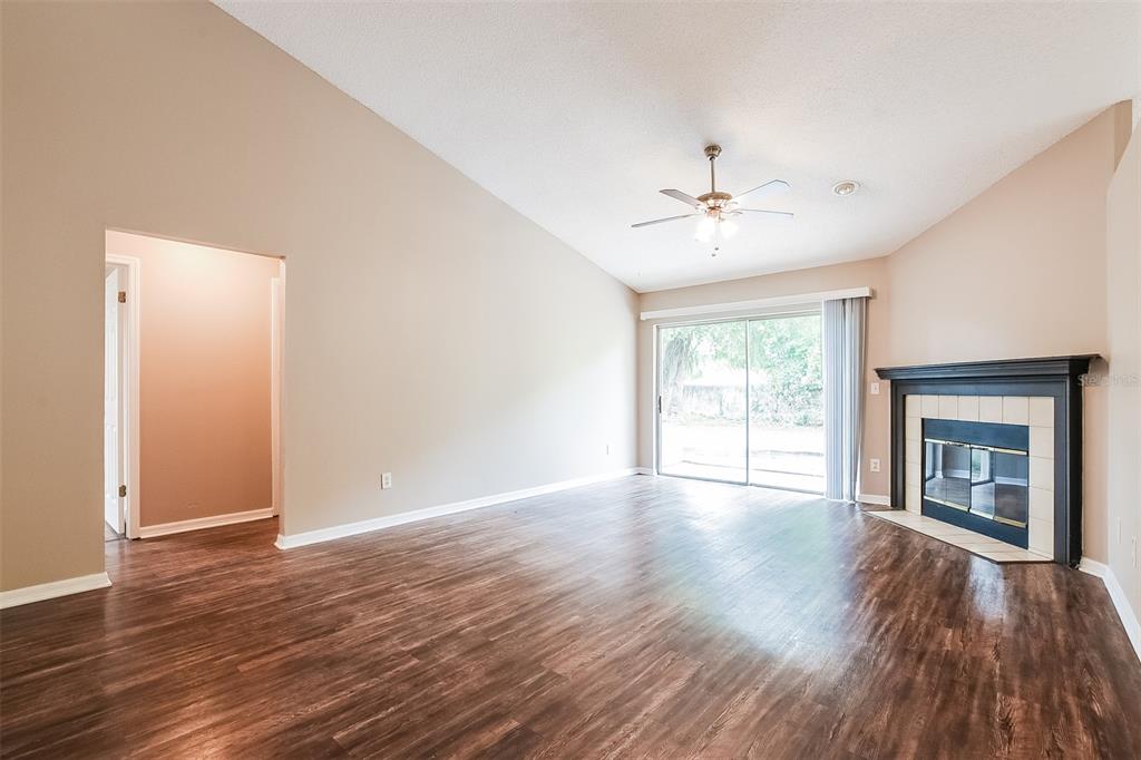 A living room with wood-look flooring, a vaulted ceiling, a ceiling fan, and a fireplace — 337 MANTIS LOOP, APOPKA, FL