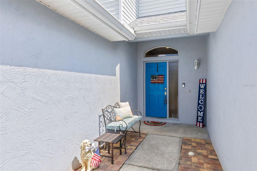 An exterior view of a home entryway featuring a blue door, a bench, and decor — 216 HEMINGWAY DRIVE, OLDSMAR, FL
