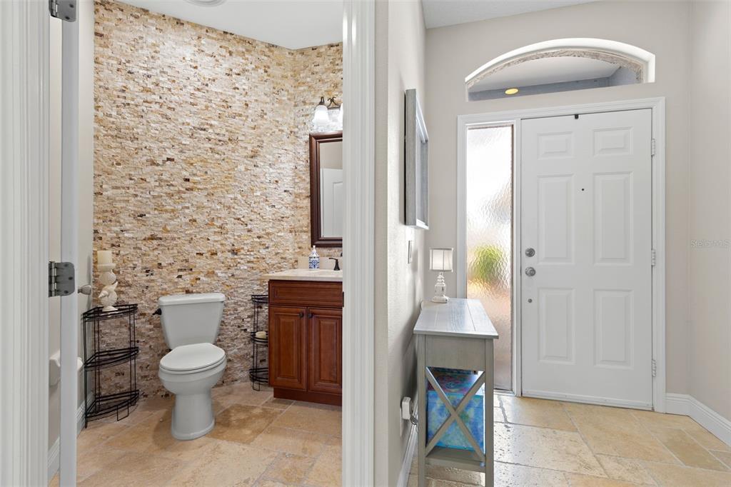 A half bathroom with a stone accent wall sits beside an entryway with a front door — 216 HEMINGWAY DRIVE, OLDSMAR, FL