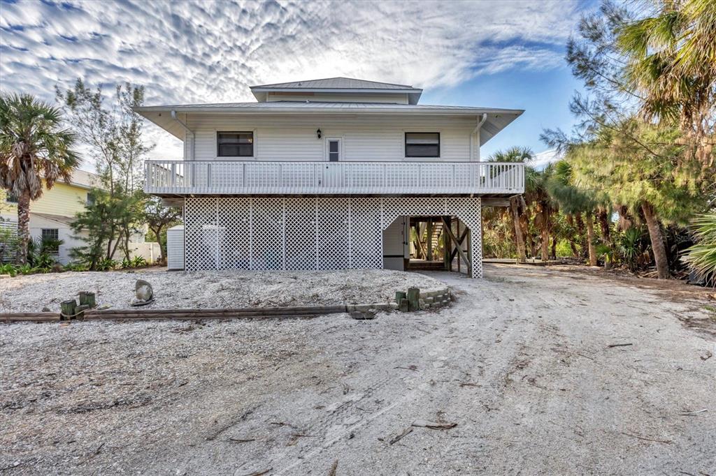 A white elevated house with a lattice-enclosed ground level sits on a sandy, shell-covered lot — 51 PALM DRIVE, PLACIDA, FL