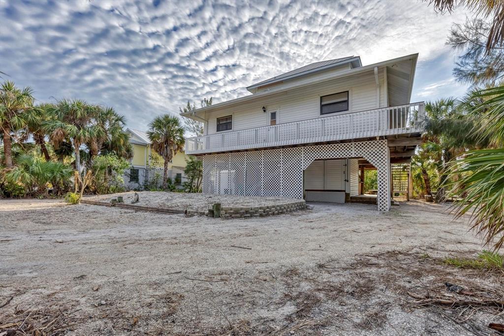 A two-story white house with a raised deck and lattice skirting stands on sandy ground — 51 PALM DRIVE, PLACIDA, FL