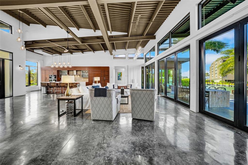 A spacious open-concept living area features polished concrete floors, a vaulted ceiling, and glass walls — 870 PARTRIDGE COURT, MARCO ISLAND, FL