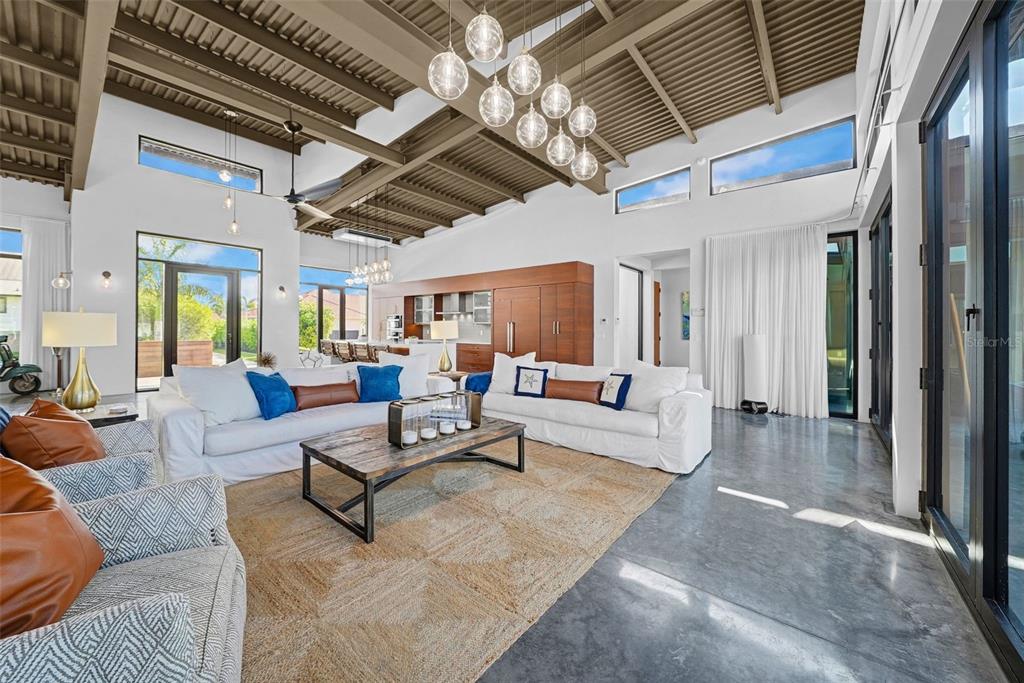 A spacious living room features a vaulted beamed ceiling, concrete floors, and a large chandelier — 870 PARTRIDGE COURT, MARCO ISLAND, FL