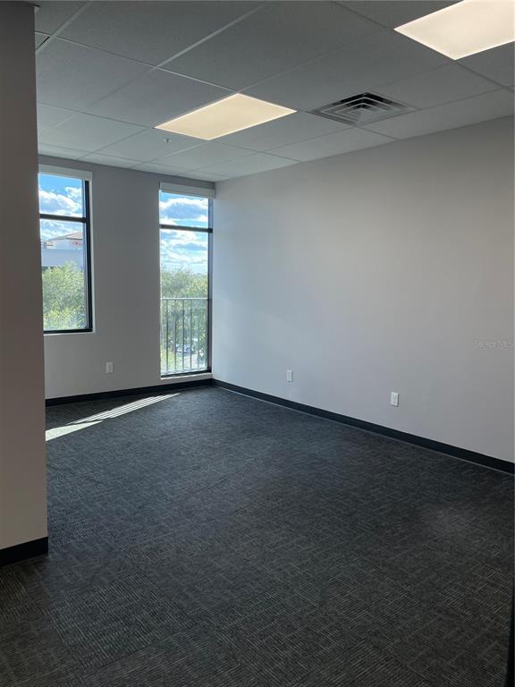 An empty office room features gray carpet, white walls, and two windows with a balcony — 13550 VILLAGE PARK DRIVE UNIT 345, ORLANDO, FL