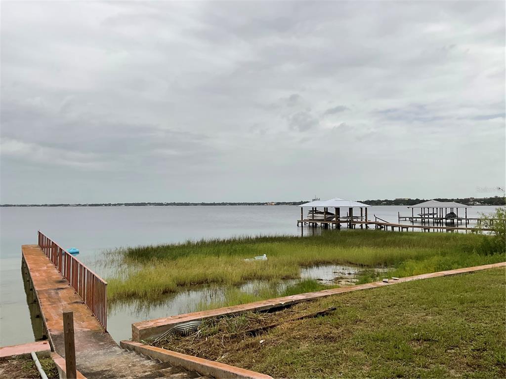 A view of a lake with a wooden dock, grassy shoreline, and two covered boat slips — 1025 LAKEVIEW DRIVE, SEBRING, FL