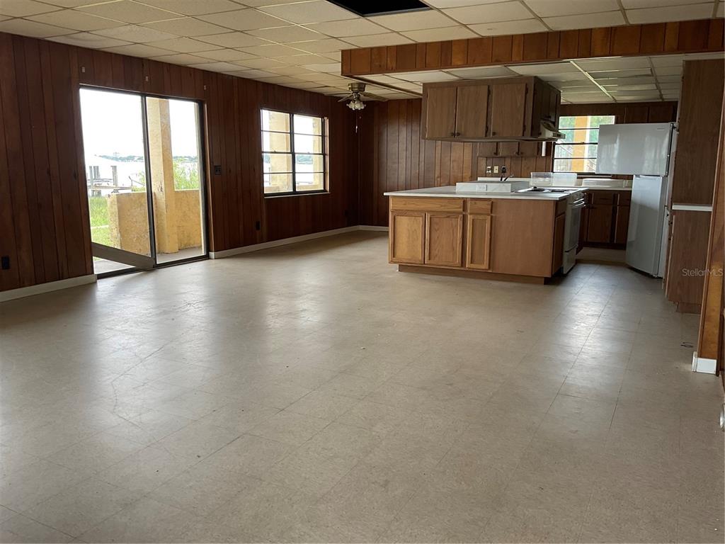 An open-concept kitchen and living area features wood paneling, drop ceilings, and a sliding door — 1025 LAKEVIEW DRIVE, SEBRING, FL