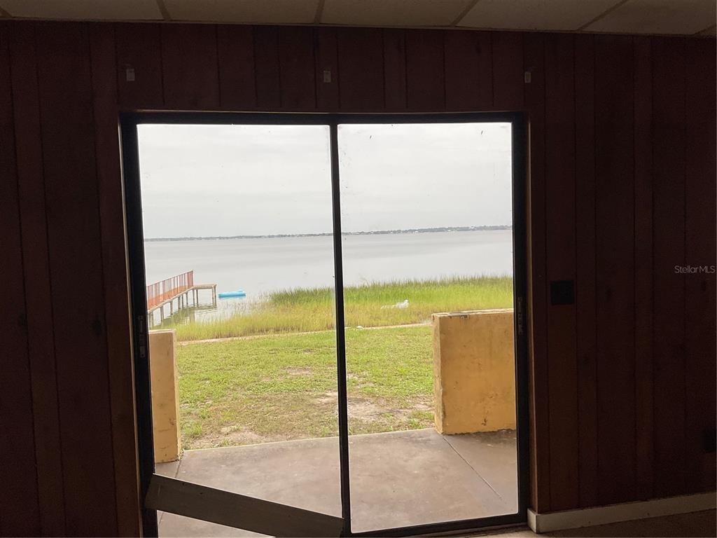 A view of a lake and dock through a sliding glass door in a wood-paneled room — 1025 LAKEVIEW DRIVE, SEBRING, FL