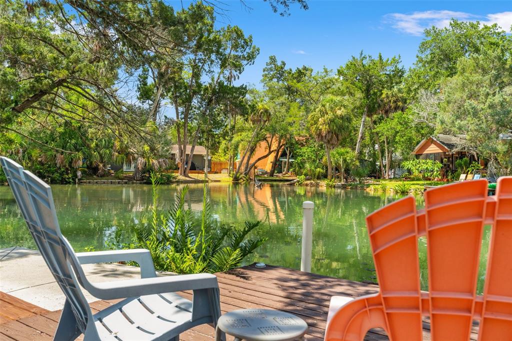 A grassy backyard features a wooden deck with chairs overlooking a calm canal — 6053 PALM CREEK DRIVE, WEEKI WACHEE, FL