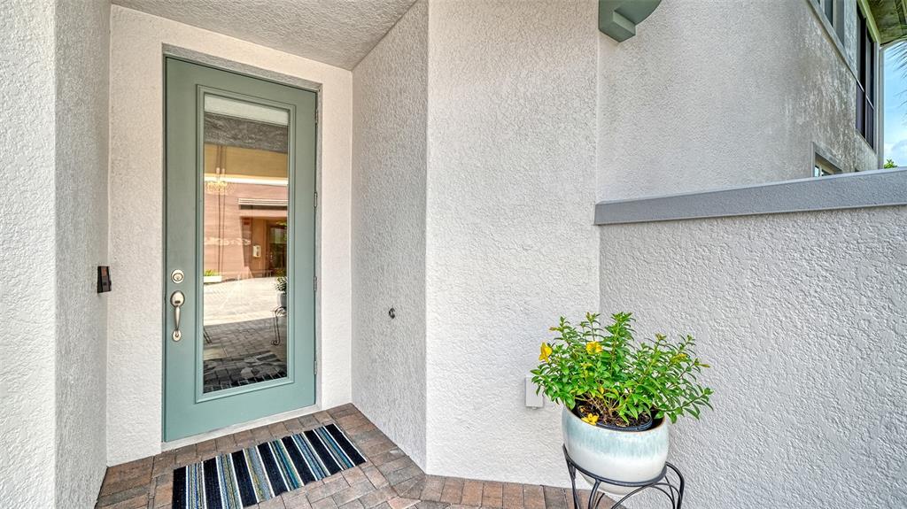 A light green front door with a glass panel sits on a paved entryway porch — 7552 DIVOT LOOP, BRADENTON, FL